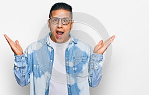 Young latin man wearing casual clothes and glasses celebrating victory with happy smile and winner expression with raised hands