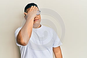 Young latin man wearing casual clothes and glasses surprised with hand on head for mistake, remember error