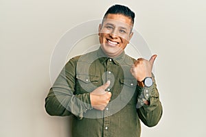 Young latin man wearing casual clothes pointing to the back behind with hand and thumbs up, smiling confident