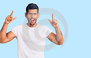 Young latin man wearing casual clothes smiling amazed and surprised and pointing up with fingers and raised arms