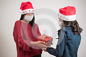 Young latin mother giving a present to her daughter on white background. Celebrating christmas wearing surgical mask during covid