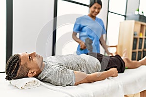 Young latin physioterapist woman make rehab treatment to hispanic man using massage gun percusion tool at the clinic