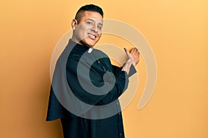Young latin priest man standing over yellow background inviting to enter smiling natural with open hand