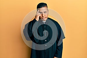 Young latin priest man standing over yellow background worried and stressed about a problem with hand on forehead, nervous and