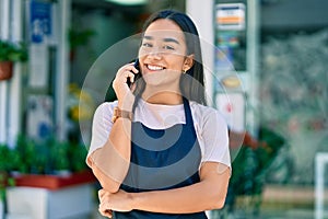 Young latin shopkeeper girl smiling happy talking on the smartphone at florist