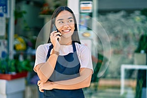 Young latin shopkeeper girl smiling happy talking on the smartphone at florist