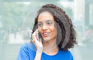 Young latin woman with curly hair at phone in city