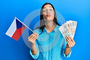 Young latin woman holding czech republic flag and koruna banknotes looking at the camera blowing a kiss being lovely and sexy