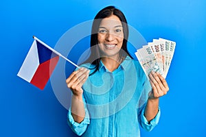 Young latin woman holding czech republic flag and koruna banknotes smiling with a happy and cool smile on face