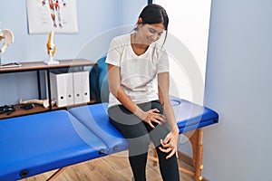 Young latin woman patient suffering for knee injury at physiotherapy clinic