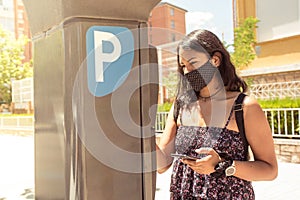 Young latin woman paying with the smartphone on the parking payment machine