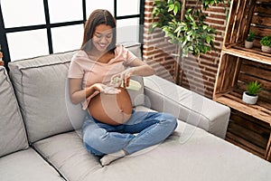 Young latin woman pregnant applying cream lotion on skin belly at home