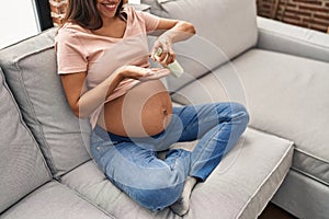 Young latin woman pregnant applying cream lotion on skin belly at home