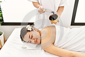 Young latin woman relaxed having back massage with chocolate therapy at beauty center
