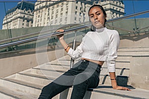 Young Latin woman sitting on the concrete staircase while enjoying the morning sun. Woman dressed in black jean and white top