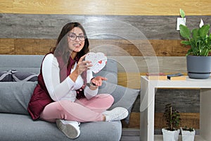 Young latin woman sitting on sofa with box of heart chocolates. Valentine`s Day