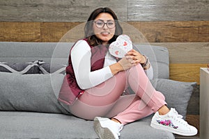 Young latin woman sitting on sofa with box of heart chocolates. Valentine`s Day