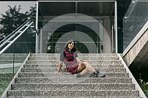 Young latin woman sitting on the stairs of a building, smiling looking at the camera with copy space
