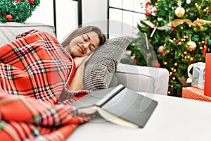 Young latin woman sleeping lying on sofa by christmas tree at home