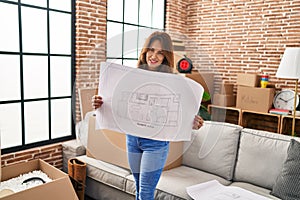 Young latin woman smiling confident holding house plan at hew home