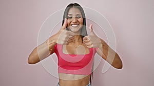 Young latin woman smiling with thumbs up over isolated pink background