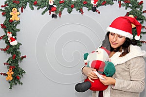 Young latin woman with sweater and santa claus hat, christmas decoration and santa claus doll