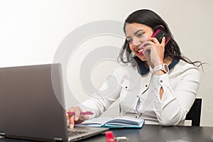 Young latin woman talking by mobile phone and working at home with the laptop. Teleworking concept on a white background photo