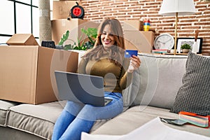 Young latin woman using laptop and credit card sitting on sofa at hew home