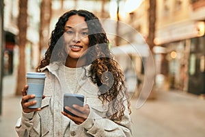 Young latin woman using smartphone and drinking coffee at the city