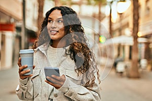 Young latin woman using smartphone and drinking coffee at the city