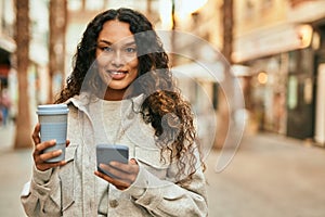 Young latin woman using smartphone and drinking coffee at the city