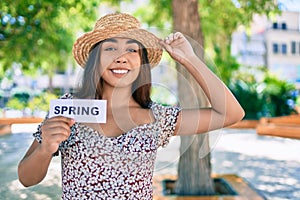 Young latin woman on vacation holding spring word paper walking at street of city