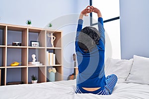 Young latin woman waking up stretching arms at bedroom