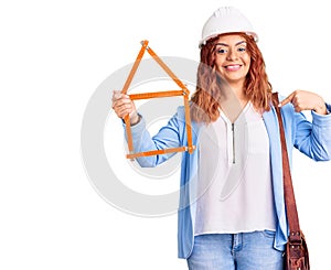 Young latin woman wearing architect hardhat pointing finger to one self smiling happy and proud