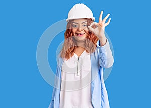 Young latin woman wearing architect hardhat smiling positive doing ok sign with hand and fingers