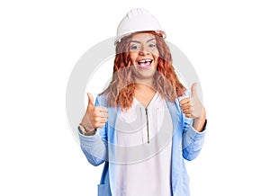 Young latin woman wearing architect hardhat success sign doing positive gesture with hand, thumbs up smiling and happy