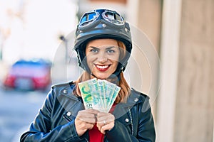 Young latin woman wearing motorcycle helmet holding israel shekels banknotes at the city