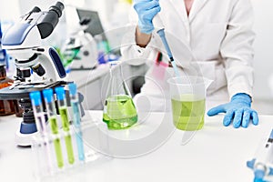 Young latin woman wearing scientist uniform pouring liquid on test tube at laboratory