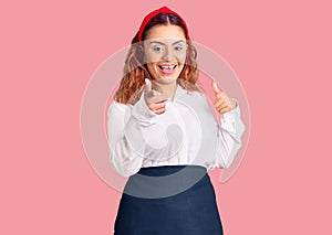 Young latin woman wearing waitress apron pointing fingers to camera with happy and funny face