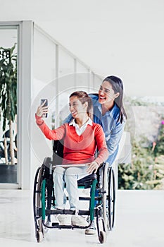 Young latin woman in wheelchair taking a selfie photo at workplace with another woman in Mexico