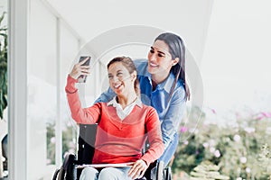 Young latin woman in wheelchair taking a selfie photo at workplace with another woman in Mexico