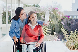 Young latin woman in wheelchair taking a selfie photo at workplace with another woman in Mexico