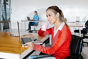 Young latin woman in wheelchair working with computer at workplace or office in Mexico city