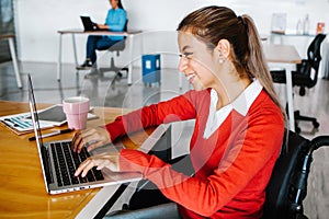 Young latin woman in wheelchair working with computer at workplace or office in Mexico city