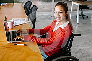 Young latin woman in wheelchair working with computer at workplace or office in Mexico city