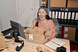 Young latin woman working at small business ecommerce angry and mad screaming frustrated and furious, shouting with anger looking