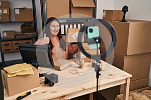 Young latin woman working at small business ecommerce doing video smiling happy and positive, thumb up doing excellent and