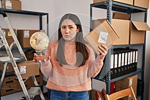 Young latin woman working at small business ecommerce doing world shipping clueless and confused expression