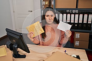 Young latin woman working at small business ecommerce packing order clueless and confused expression