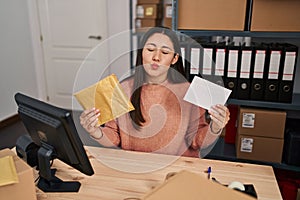 Young latin woman working at small business ecommerce packing order looking at the camera blowing a kiss being lovely and sexy